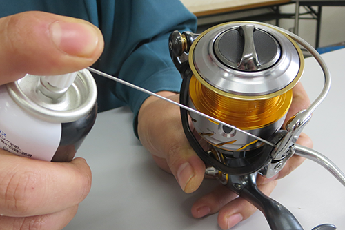 スピニングリールのベール可動部にスプレーグリスを吹き付けている手元
