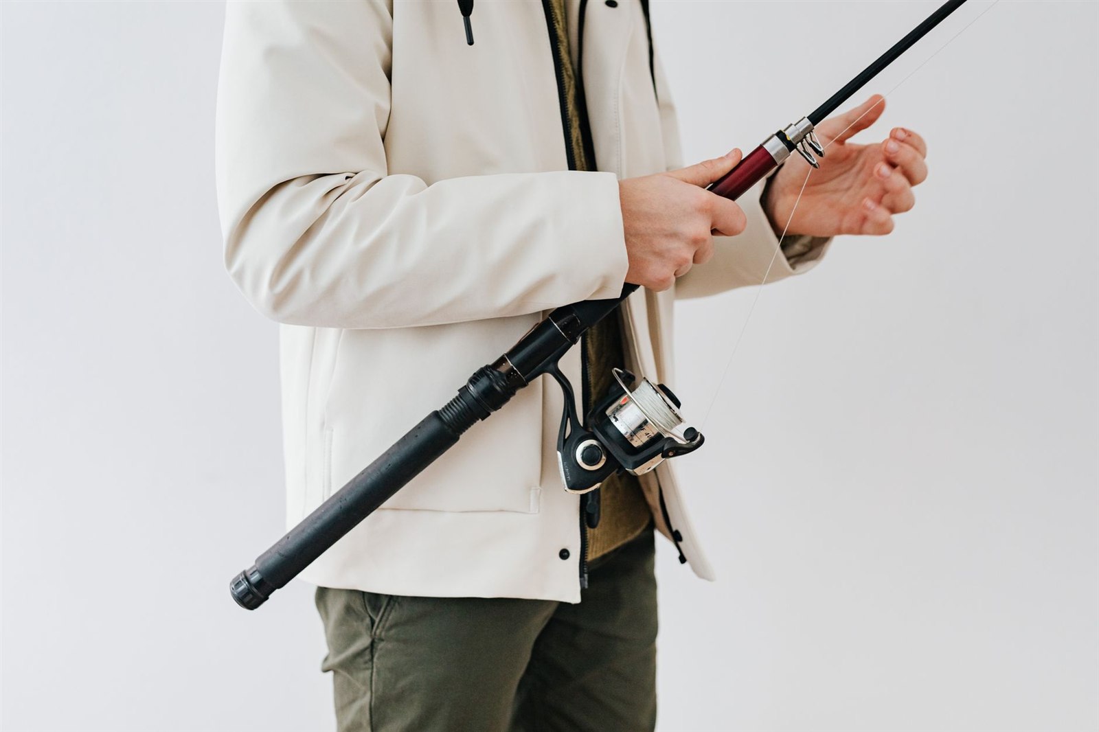 白い上着の人が、スピニングリールを付けた振出竿を持ち、赤い節と細い節の継ぎ目の手前を握っている。もう片方の手にはラインが掛かっている